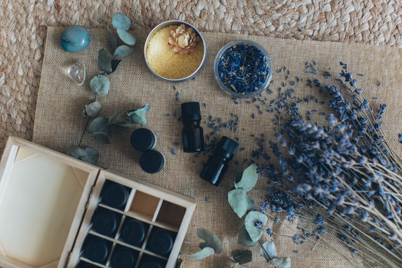 A flat lay displaying essential oils, dried lavender, and other aromatherapy items on a woven mat.