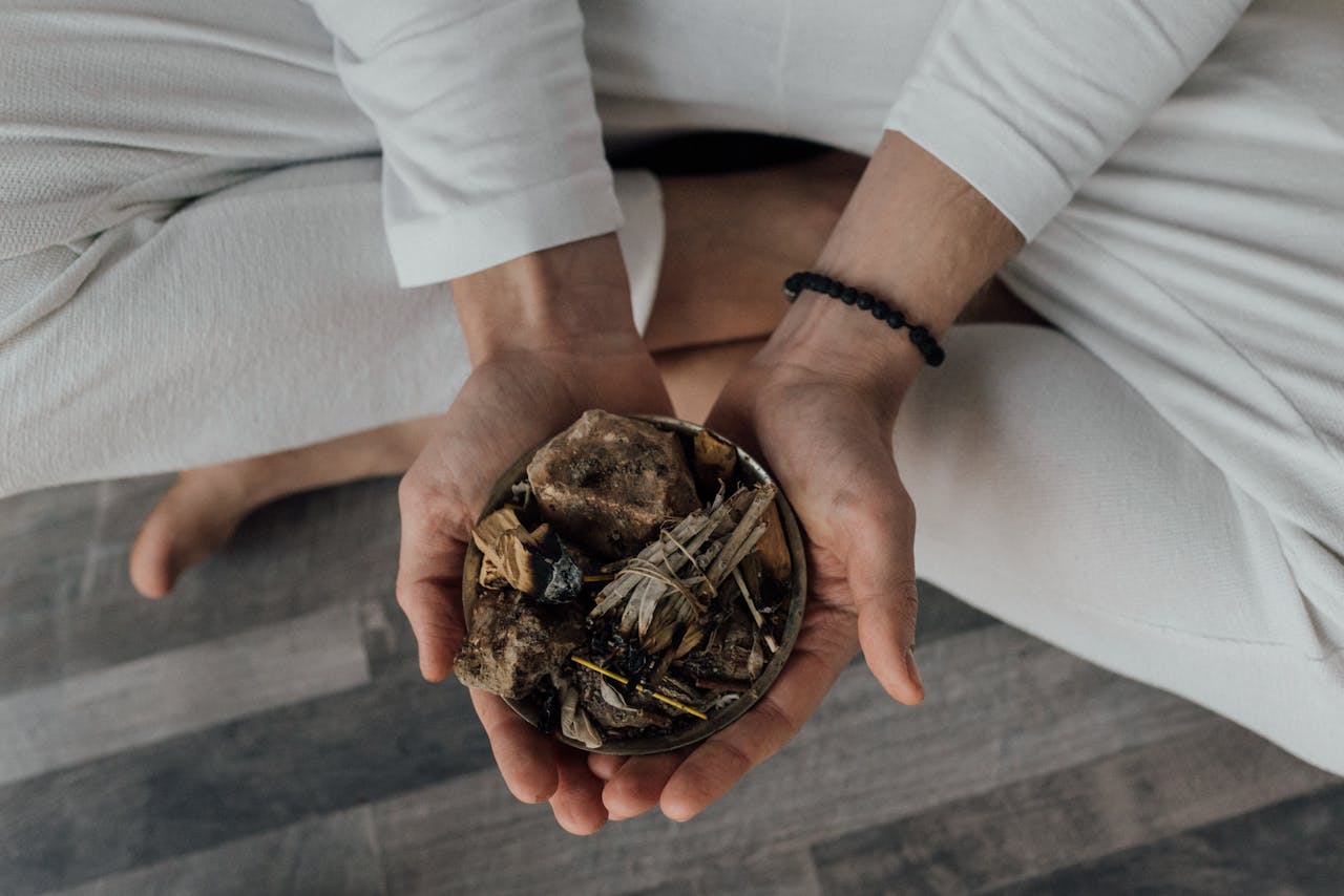 Hands in meditation pose holding a bowl with incense and herbs, promoting tranquility.